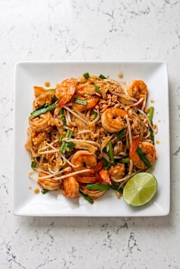 Plate of Shrimp Pad Thai with rice noodles, shrimp, bean sprouts, peanuts, and lime wedge.