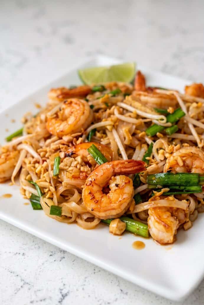 Shrimp Pad Thai with shrimp, rice noodles, bean sprouts, tofu, peanuts, and lime wedges.