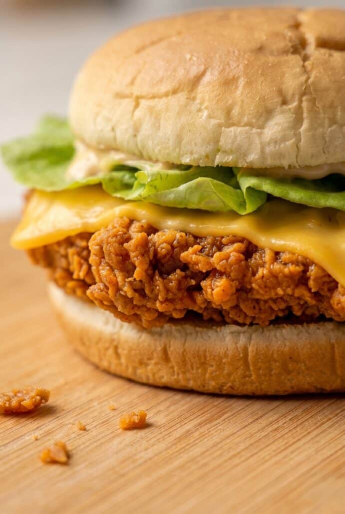 Close-up of spicy fried chicken burger with crispy chicken, cheese, and lettuce on a bun.