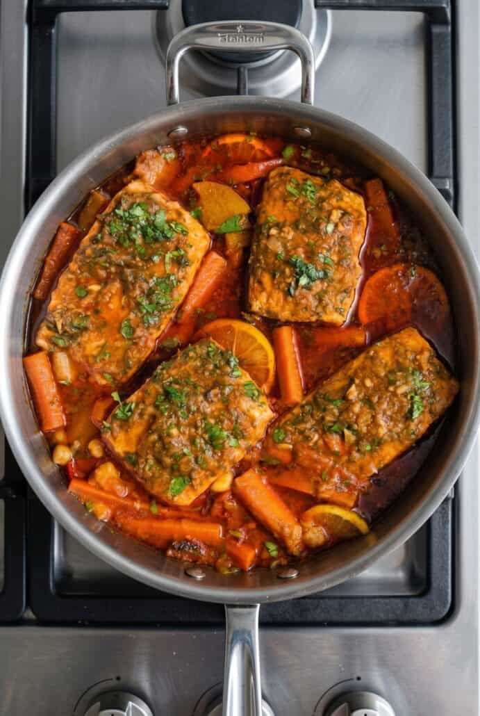 Spicy Moroccan fish simmering in a skillet with salmon, carrots, peppers, cilantro, and paprika sauce.