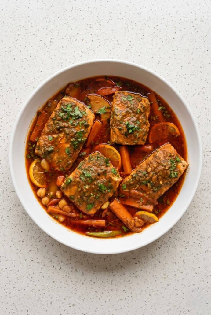 Bowl of Spicy Moroccan fish with salmon, vegetables, cilantro, and rich paprika sauce.