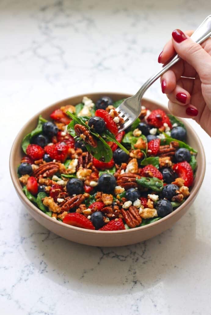 Serving strawberry spinach salad with blueberries, feta, pecans, and balsamic glaze for a fresh summer meal.