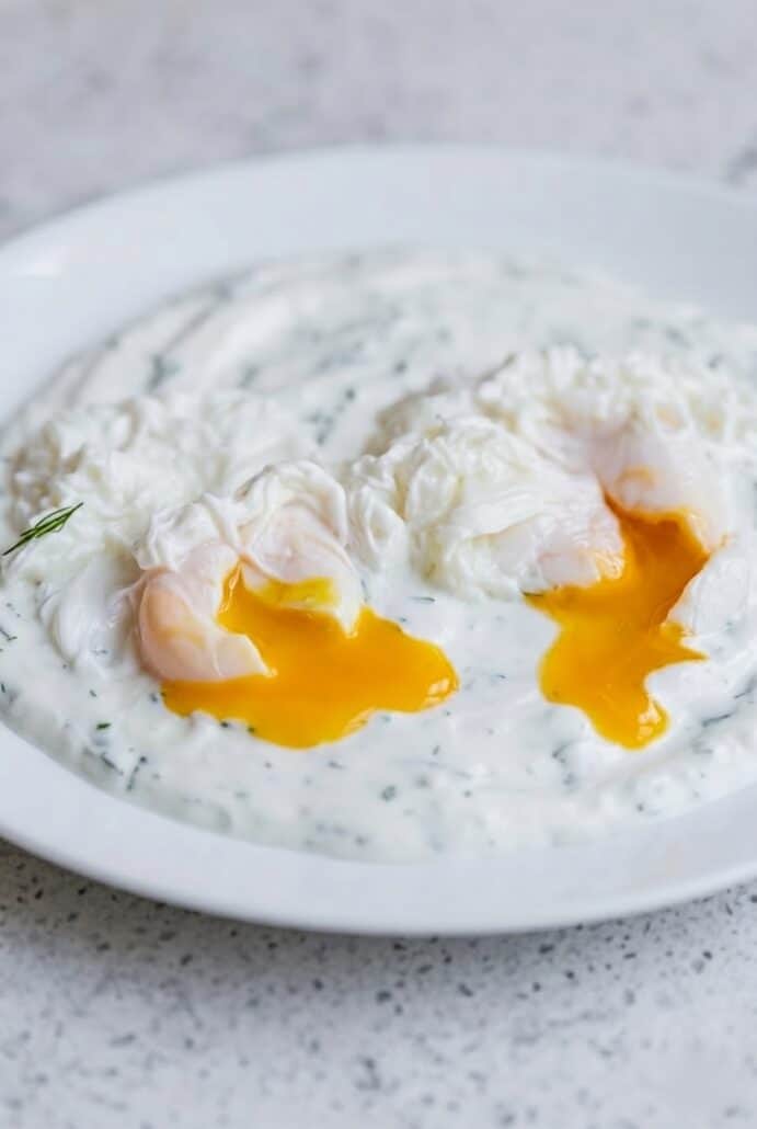 Poached eggs with runny yolks on creamy garlic yogurt for Turkish eggs Cilbir recipe.