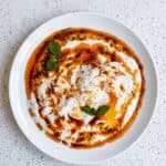 Turkish eggs with poached eggs, garlic yogurt, fresh herbs, and spiced butter sauce.
