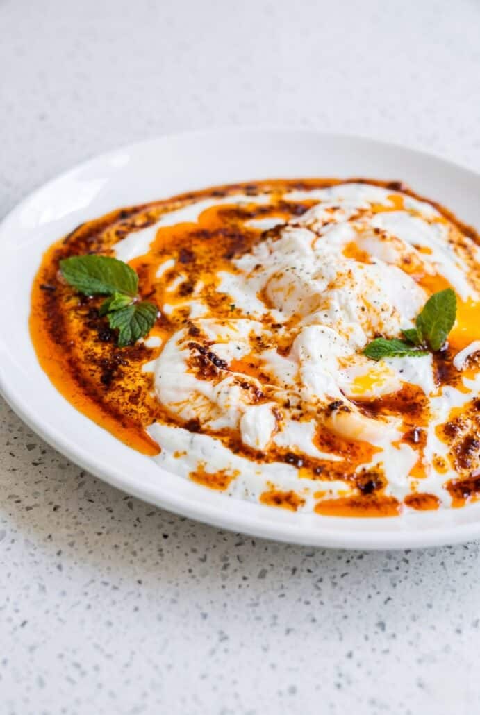 Close-up of Turkish eggs with creamy garlic yogurt, fresh mint, and spiced butter.