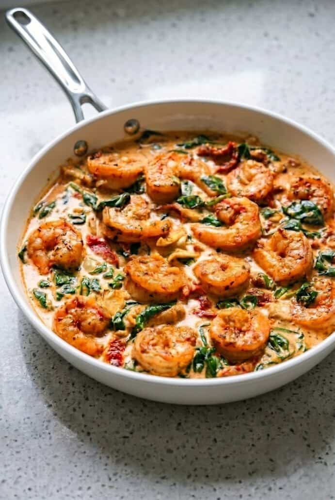 Creamy Tuscan shrimp in a skillet with spinach, artichokes, and sun-dried tomatoes.