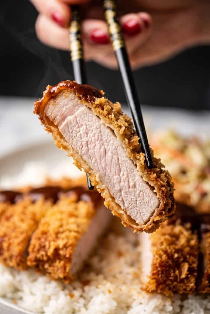 Piece of crispy Chicken Katsu held with chopsticks showing juicy chicken inside the crunchy panko coating.