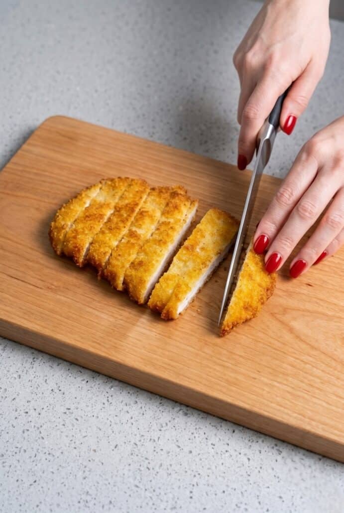 Slicing crispy Chicken Katsu on a cutting board before serving.