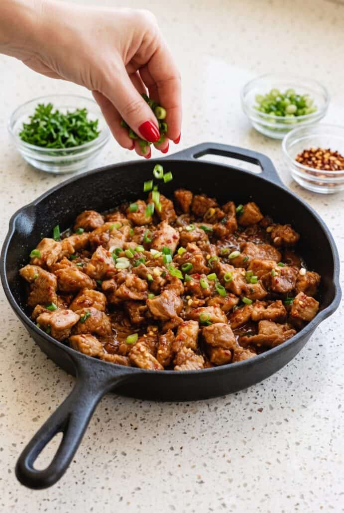 Garlic pork stir-fry in a skillet topped with fresh scallions before serving.