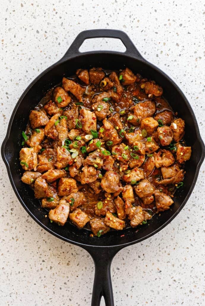 Delicious sticky garlic pork stir-fry in a black skillet with green onions.