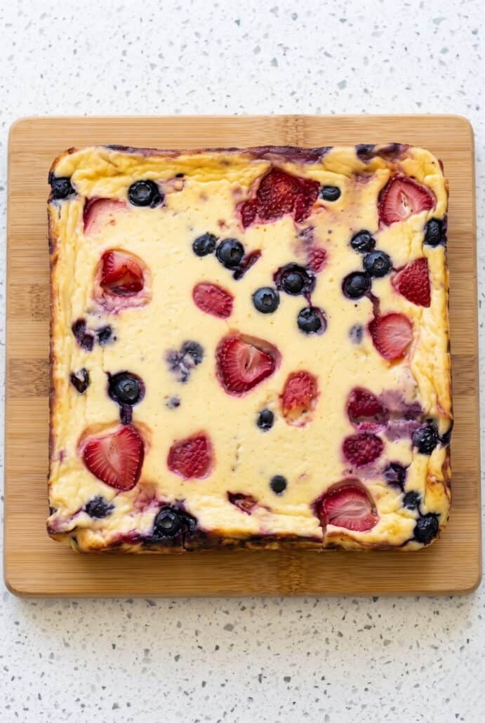 Freshly baked yogurt with strawberries, blueberries, and raspberries in a square baking dish.