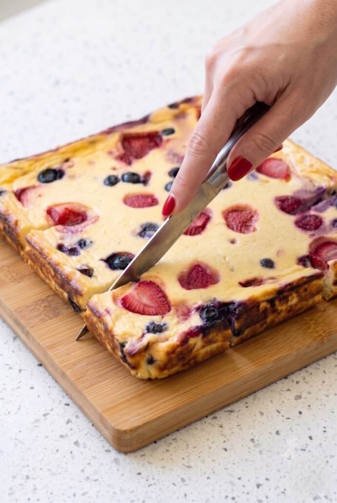 Slicing a berry baked yogurt breakfast into squares on a wooden board.