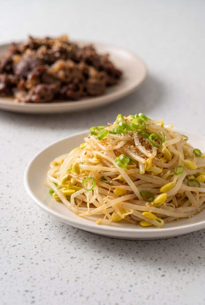 Korean bean sprout salad served as a crunchy side dish with beef in the background.