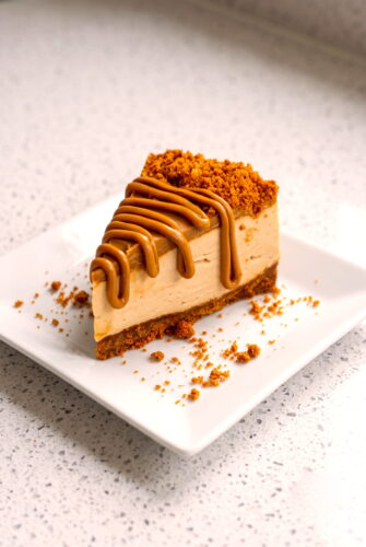 No-Bake Biscoff Cheesecake Recipe Slice of creamy Biscoff cheesecake with melted Biscoff spread drizzle and crushed Biscoff topping.