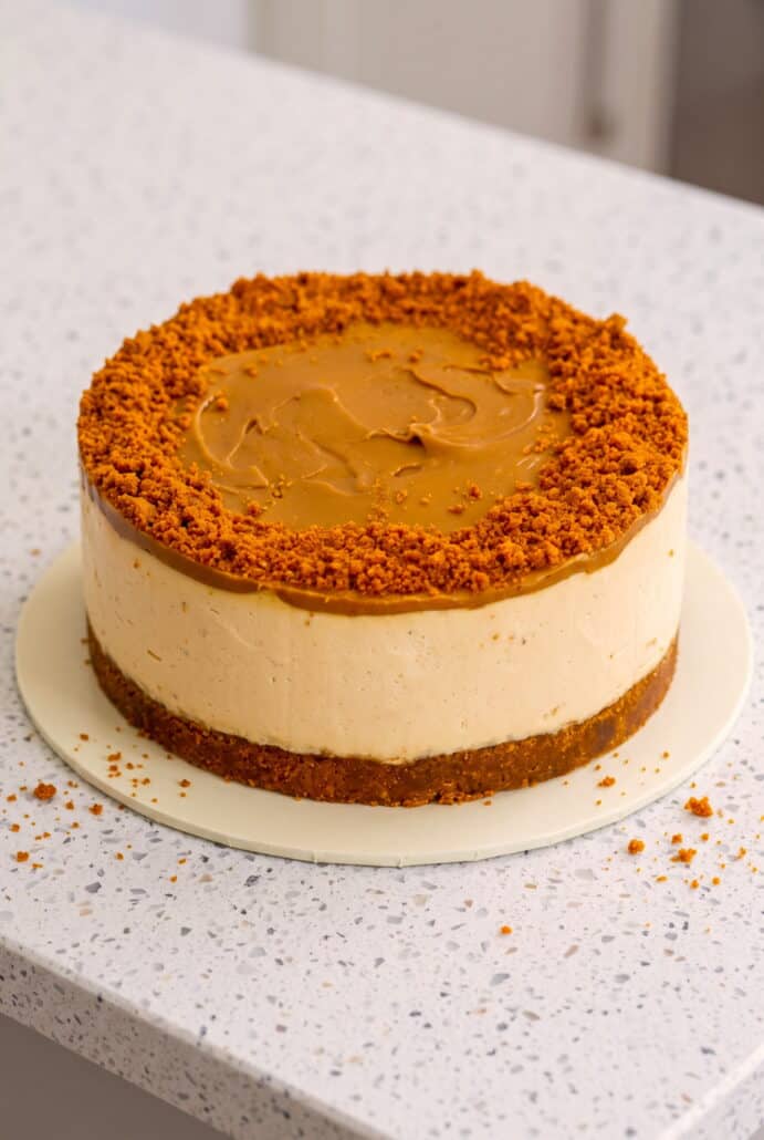 Whole no-bake Biscoff cheesecake topped with melted cookie butter and crushed biscuits.