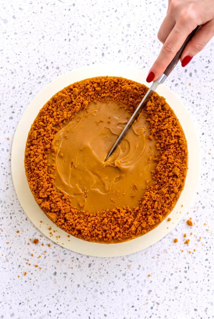 Biscoff cheesecake being sliced, topped with melted cookie butter and crushed biscuits.