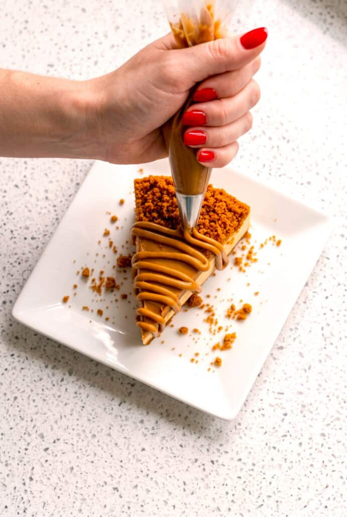 Hand cutting into a slice of Biscoff cheesecake drizzled with melted Biscoff spread.