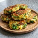 Broccoli cheese patties stacked on a wooden board, showing the crispy stovetop recipe ready to serve.