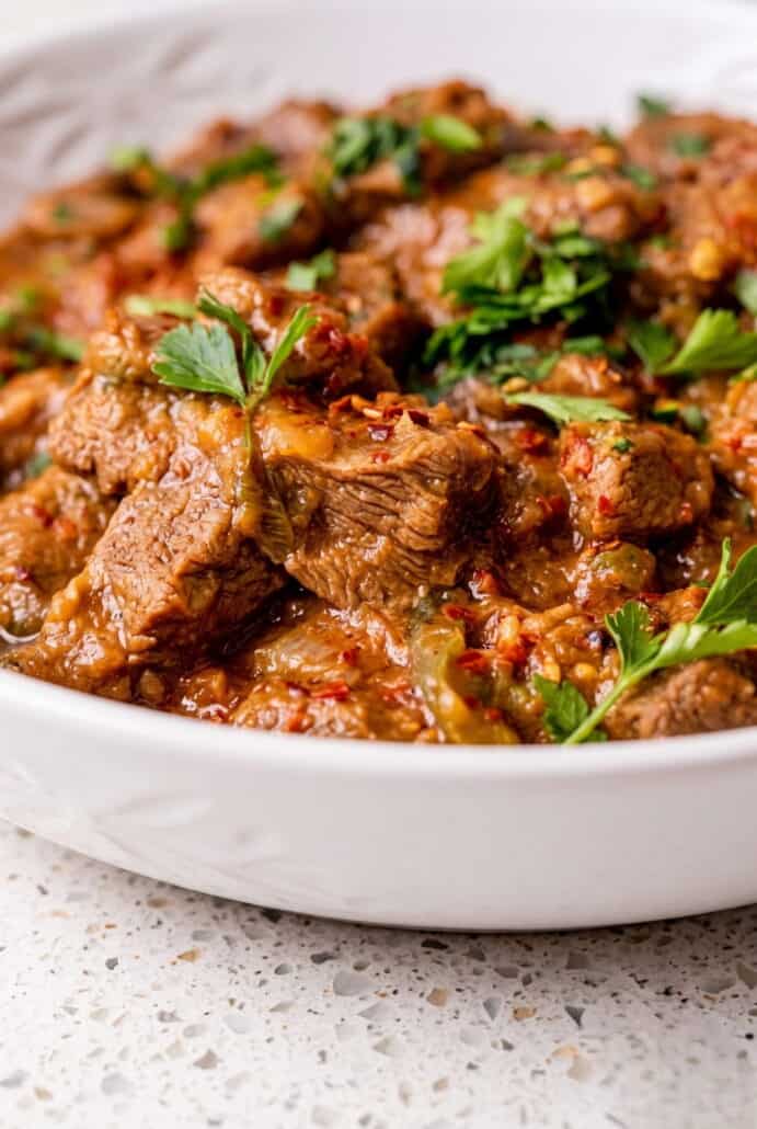 Close-up of tender carne guisada beef chunks in rich tomato gravy with fresh cilantro.