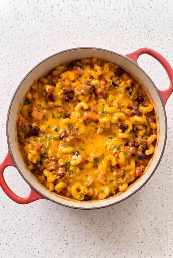Cheesy chili mac with ground beef and macaroni baked in a red-handled casserole dish.