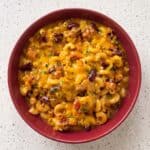 Cheesy homemade chili mac with ground beef, macaroni, and parsley in a red bowl.