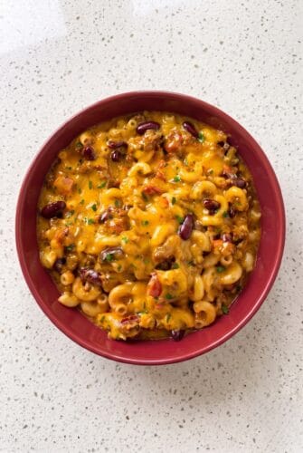 One Pot Chili Mac Recipe Cheesy homemade chili mac with ground beef, macaroni, and parsley in a red bowl.
