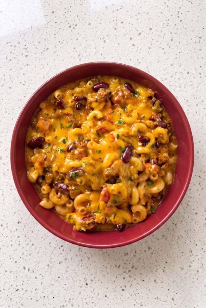 Cheesy homemade chili mac with ground beef, macaroni, and parsley in a red bowl.