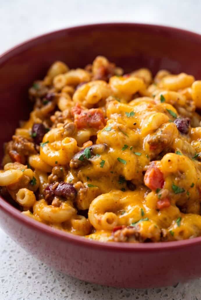 Bowl of homemade chili mac with ground beef, elbow macaroni, melted cheddar, and parsley.