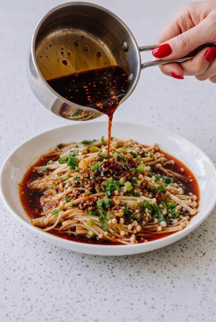 Pouring warm garlic and scallion sauce over blanched enoki mushrooms before serving.