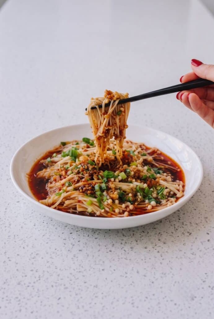 Lifting enoki mushrooms with chopsticks to show their tender texture and savory garlic scallion sauce.
