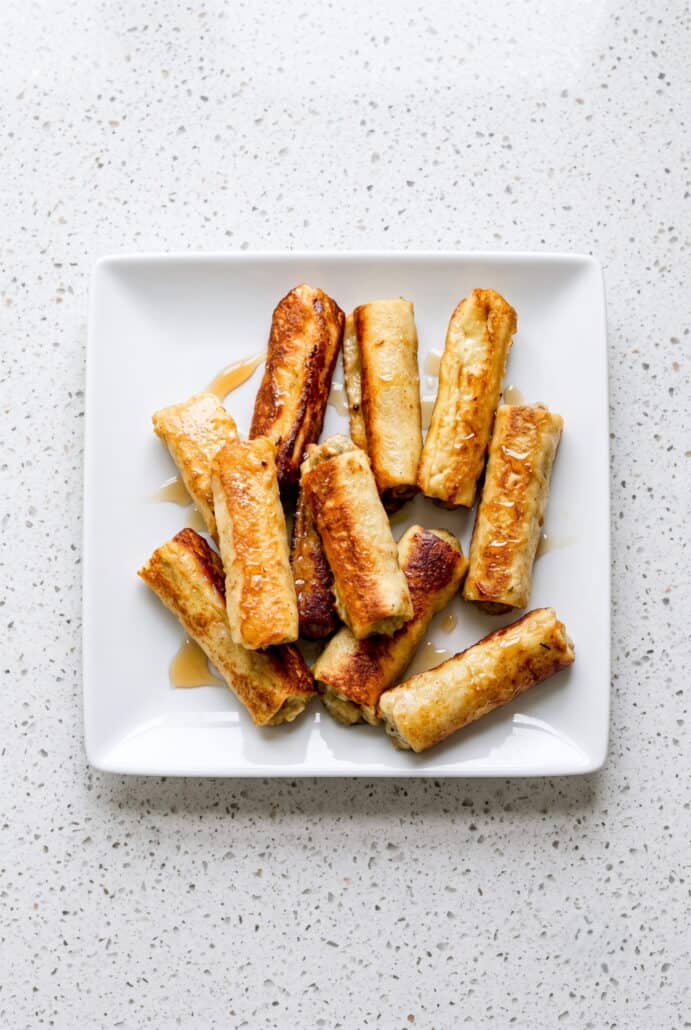Golden French toast roll-ups stacked on a plate for an easy sausage breakfast.