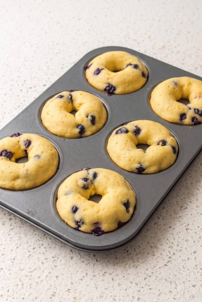 Freshly baked lemon blueberry donuts cooling in a donut pan.