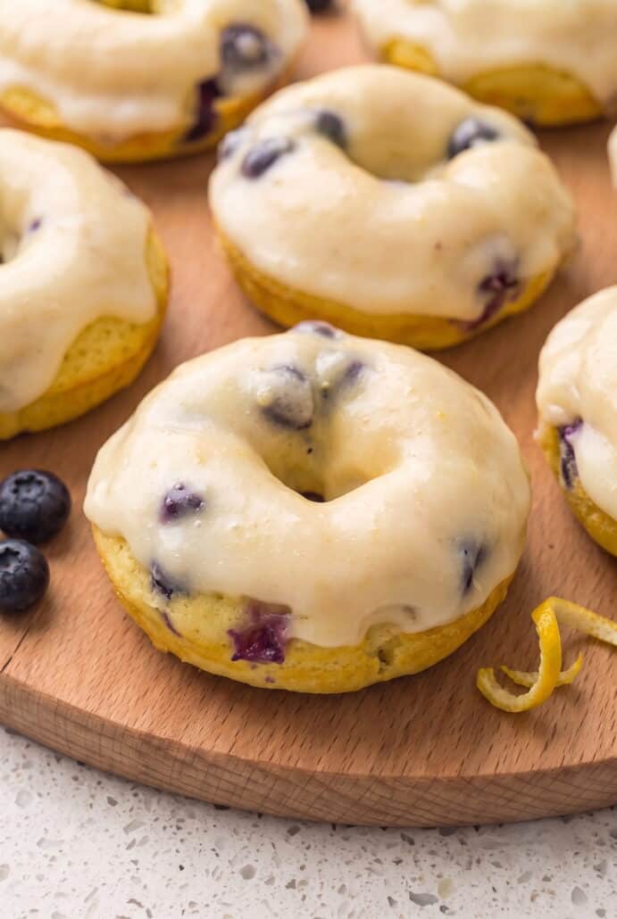 Close-up of a glazed lemon blueberry donut with fresh blueberries and lemon zest.