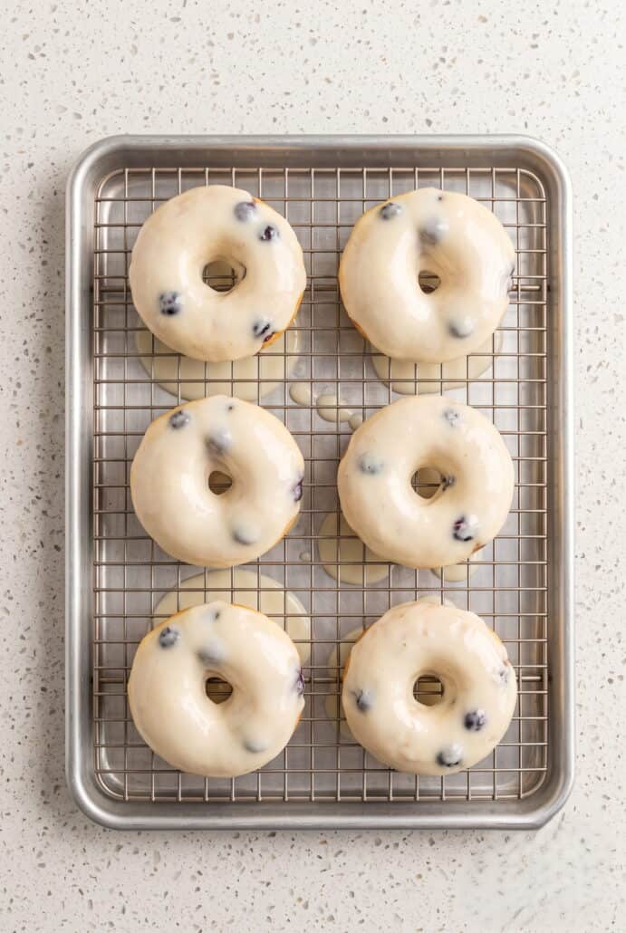 Glazed lemon blueberry donuts cooling on a wire rack.