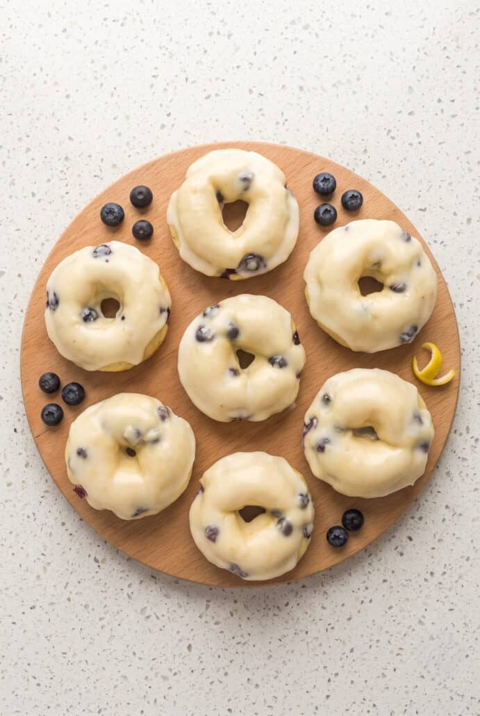 Glazed lemon blueberry donuts arranged with fresh blueberries and lemon zest.