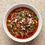 Mexican birria crockpot stew topped with chopped onion and cilantro in a rich red consommé.