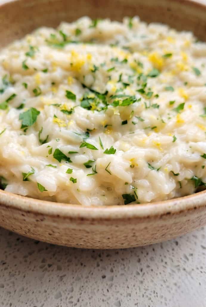 Close-up of creamy Parmesan rice garnished with chopped parsley and lemon zest.