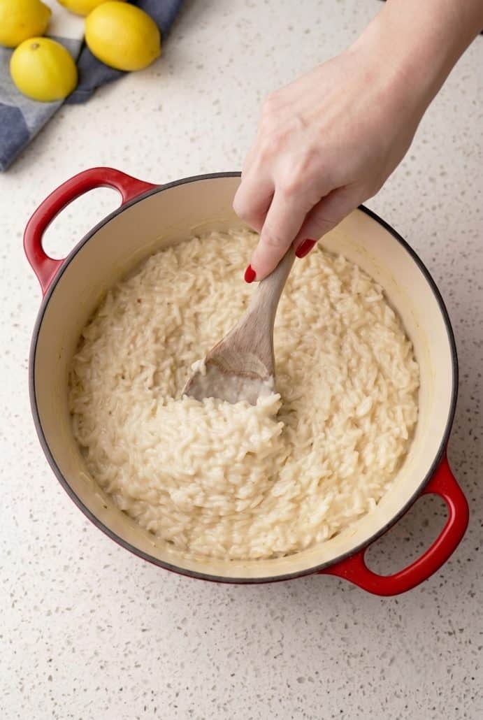 Stirring creamy Parmesan rice in a red Dutch oven on the stovetop.