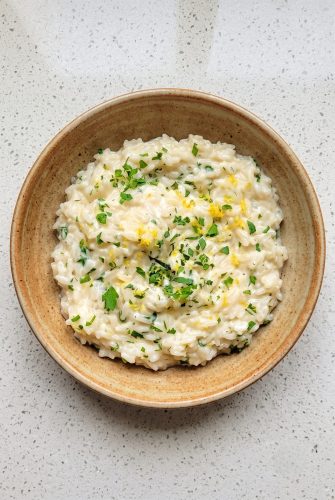 Creamy Cheesy Parmesan Rice Recipe (Easy Side Dish) Creamy Parmesan rice topped with parsley and lemon zest in a wooden bowl.