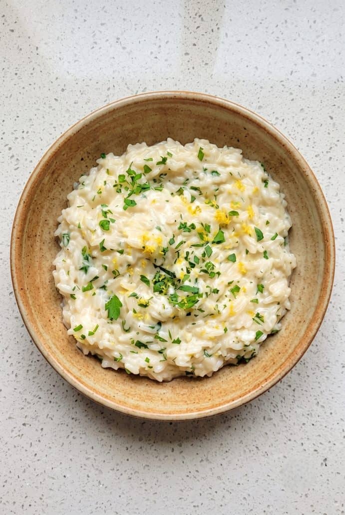 Creamy Parmesan rice topped with parsley and lemon zest in a wooden bowl.