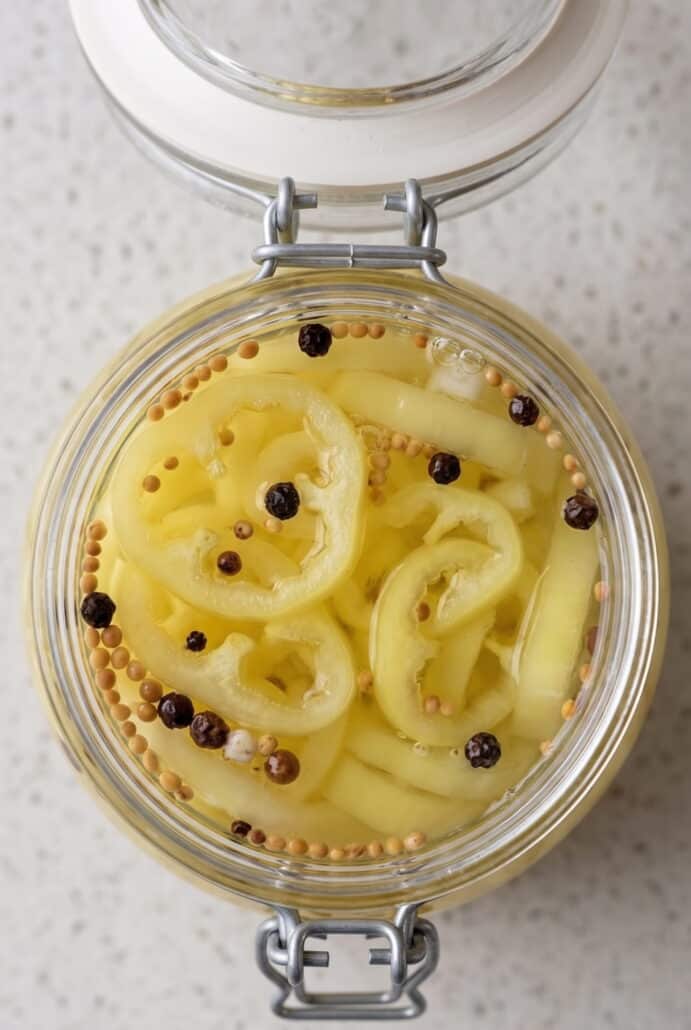 Sliced pickled banana peppers submerged in brine with garlic and whole spices.