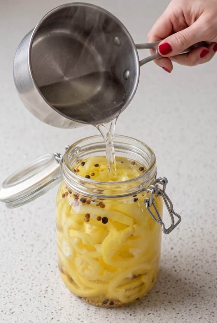 Pouring hot pickling brine over sliced banana peppers in a mason jar.