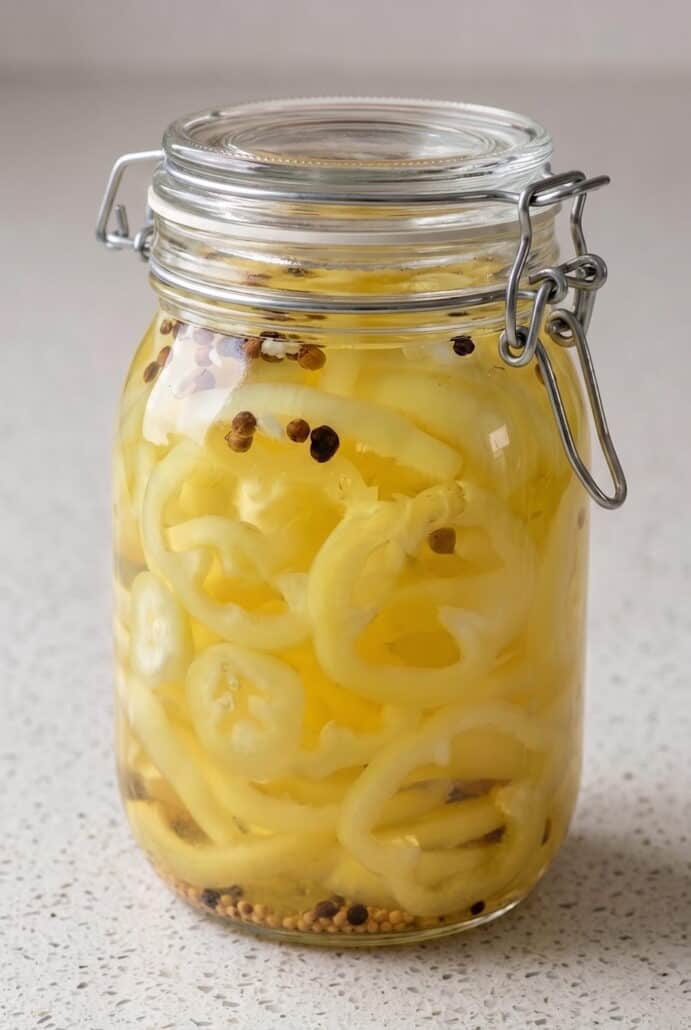 Homemade pickled banana peppers in a glass jar with garlic and whole spices.