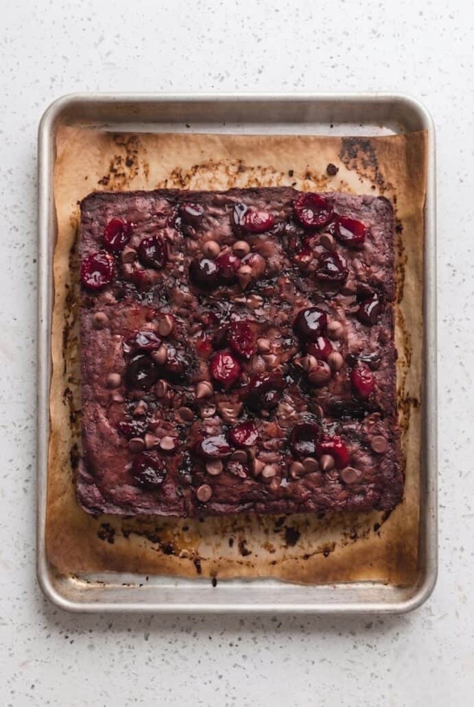 Roasted cherry brownies cooling in a parchment-lined square baking pan.