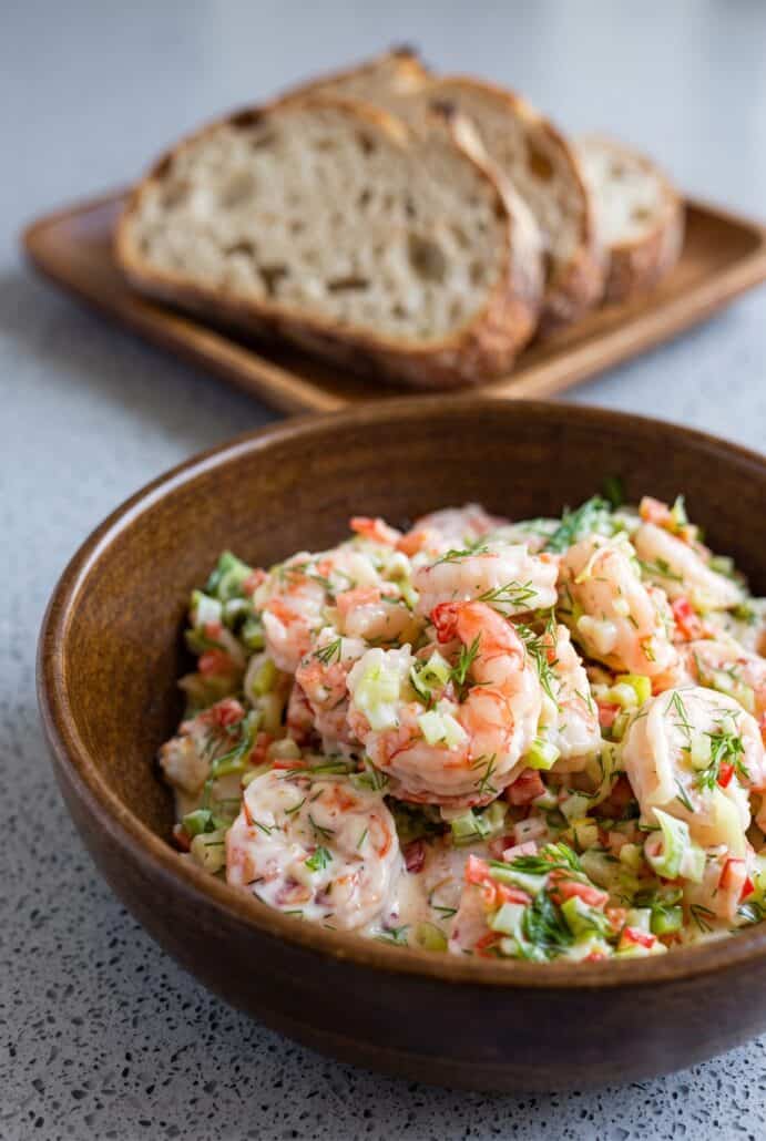 Shrimp salad with fresh dill and vegetables served in a wooden bowl.