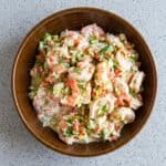 Creamy shrimp salad with dill, celery, and red bell pepper in a wooden bowl.