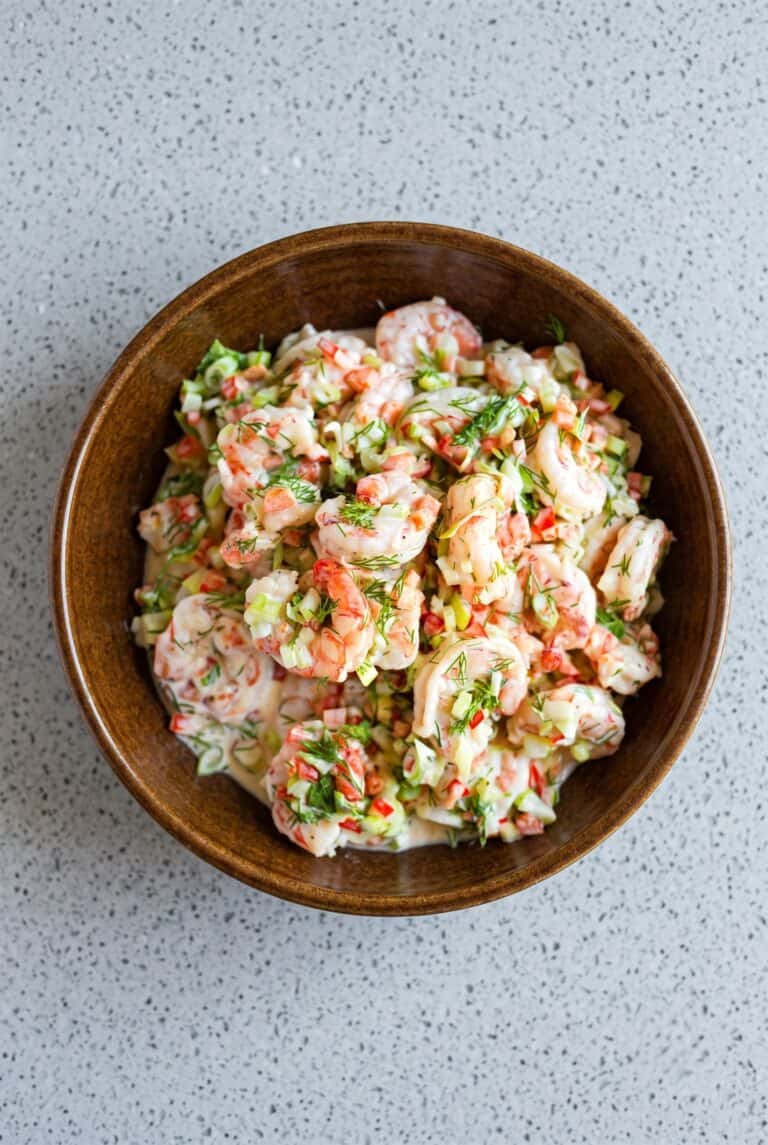 Creamy shrimp salad with dill, celery, and red bell pepper in a wooden bowl.
