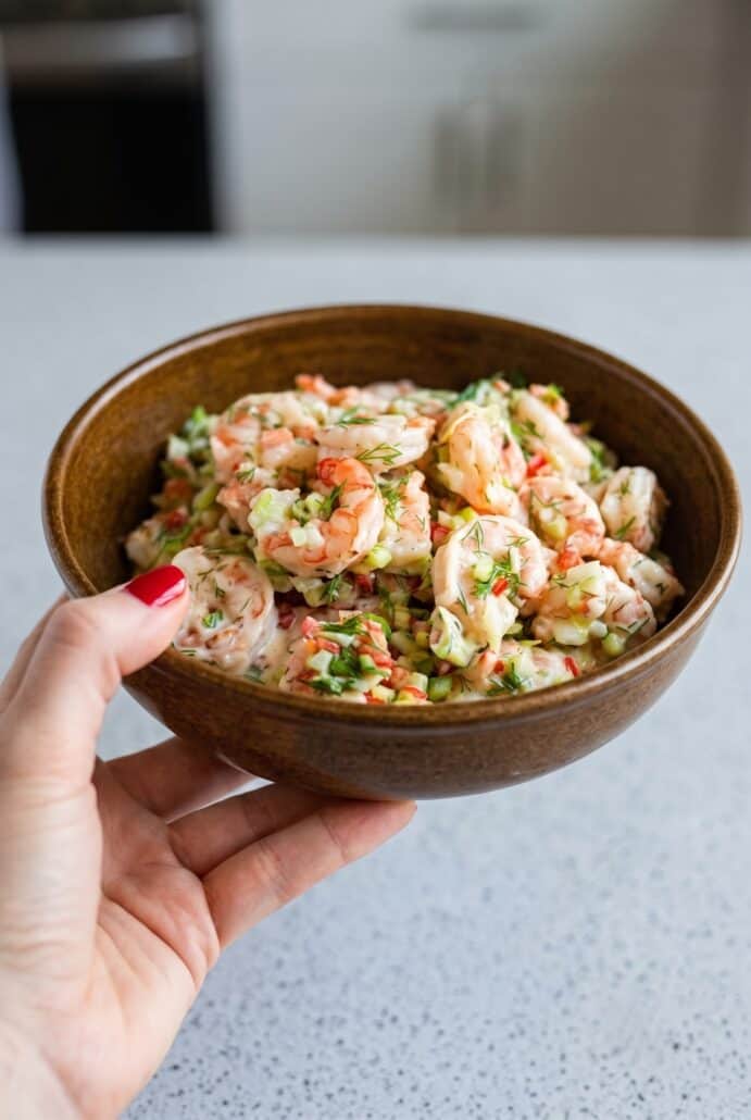 Creamy shrimp salad with dill and vegetables served in a wooden bowl.