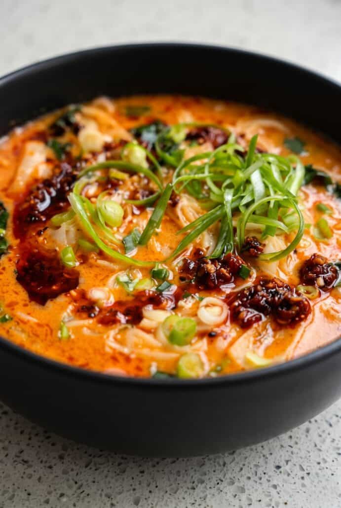 Spicy coconut noodles in creamy broth topped with chili oil, scallions, and fresh herbs.