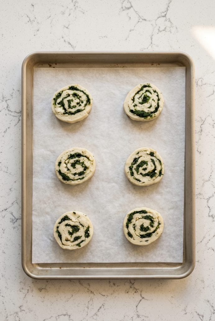 Unbaked spinach feta puff pastry pinwheels arranged on a parchment-lined baking sheet before chilling and baking.